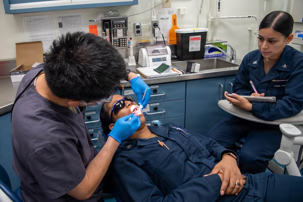 260826-N-CR055-1046 U.S. Navy Personnel Specialist 1st Class Shanekie Miller, middle, receives a dental exam from Commander Jerry Cheng, left, as Hospital Corpsman 2nd Class Carina Torres takes notes in the dental department aboard USS Ronald Reagan (CVN 76), while in port at Naval Base Kitsap-Bremerton, Washington, Aug. 26, 2026. The Nimitz-class aircraft carrier Ronald Reagan is undergoing scheduled maintenance at Puget Sound Naval Shipyard and Intermediate Maintenance Facility while remaining a combat-ready force dedicated to protecting and defending the United States. (U.S. Navy photo by Mass Communication Specialist 3rd Class Kleighton Vitug)