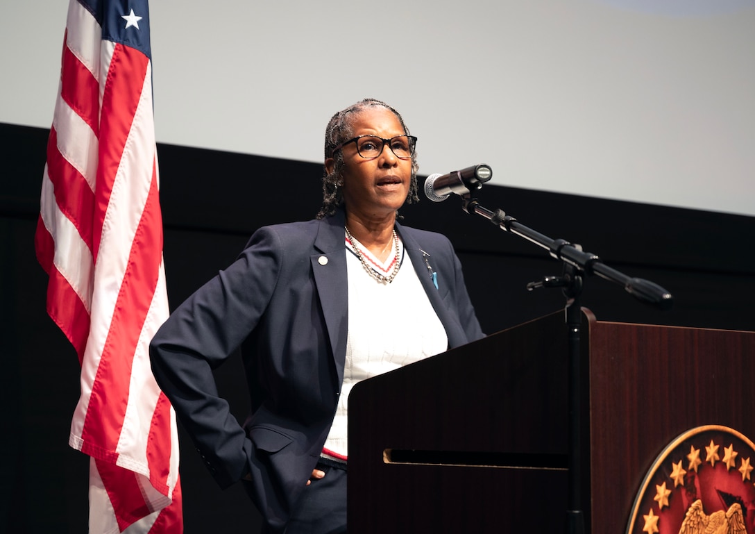 Smiling woman wears a dark suit and glasses and stands behind a podium