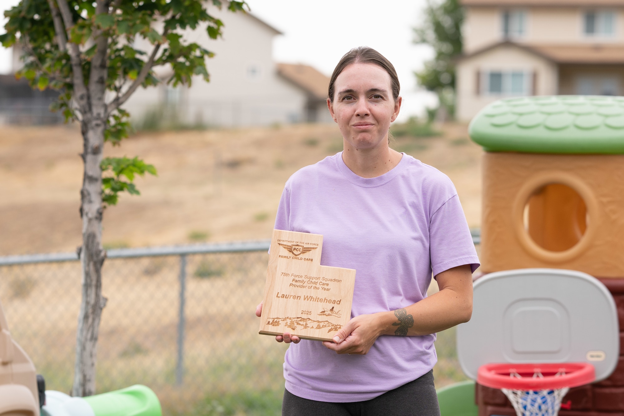 Whitehead stands in her backyard holding her wooden 2025 Family Child Care Provider of the Year plaque, which is in the shape of the state of Utah.