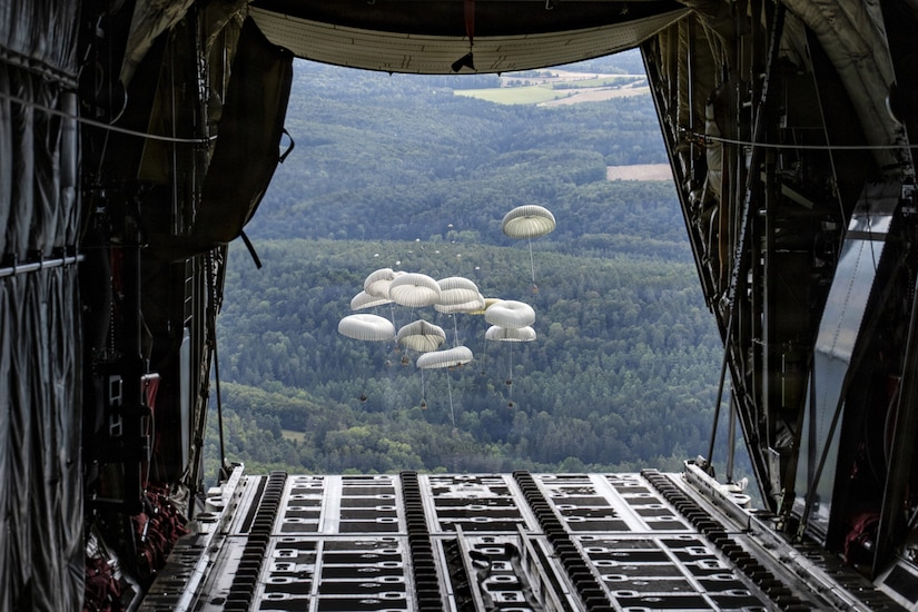 Packages parachute to the ground in a wooded area after being dropped from a military aircraft.