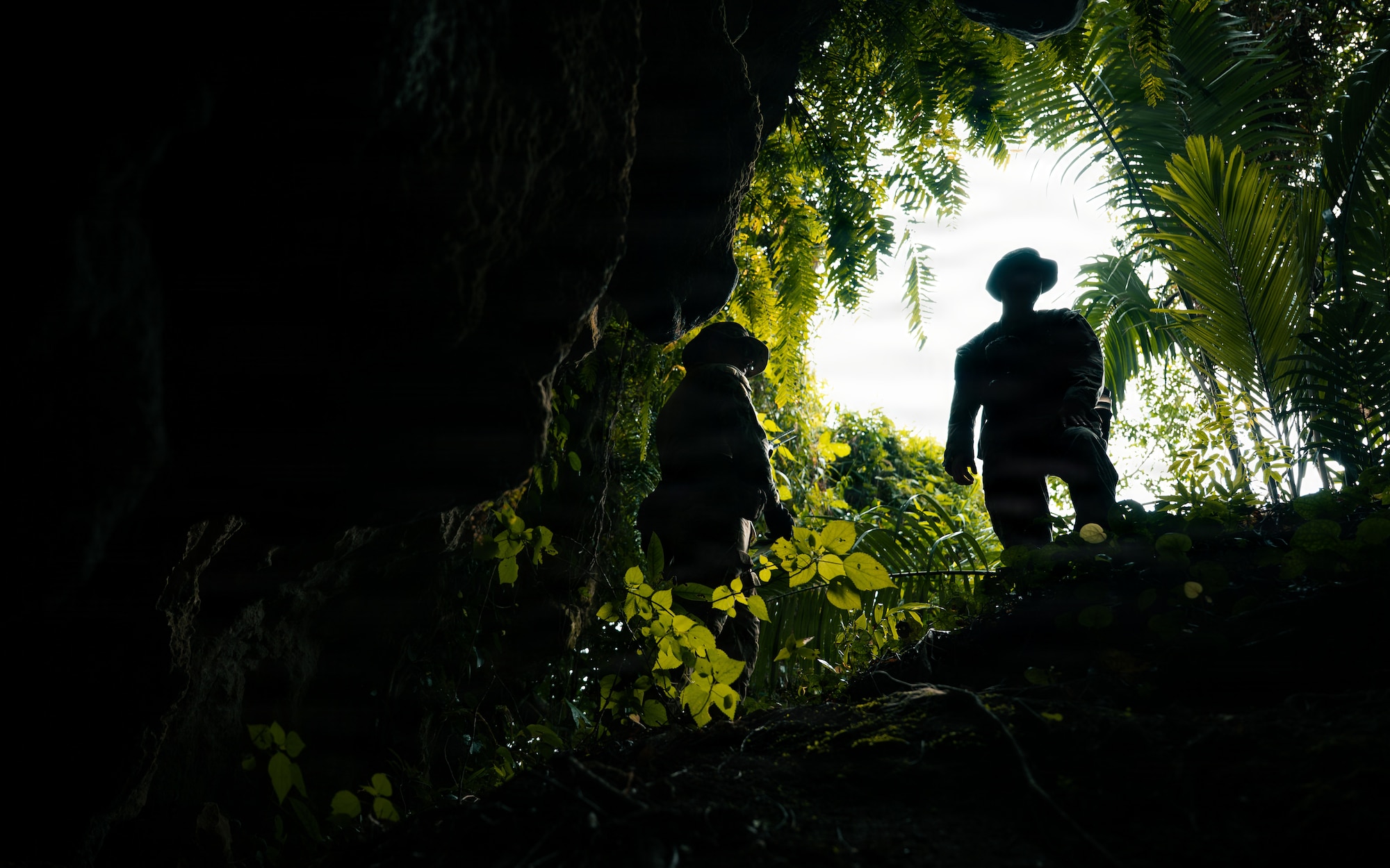 A person watches EOD members search a cave for simulated unexploded ordnance.