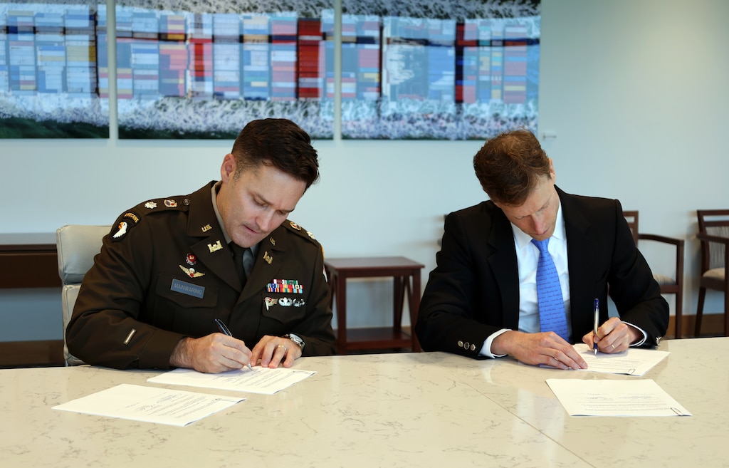 Two men sit at a table and sign an agreement.