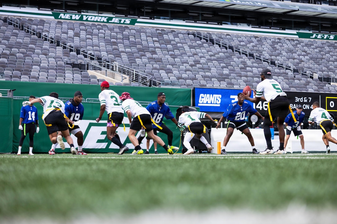A turf view of service members, civilians and families playing flag football with an empty stadium in the background.
