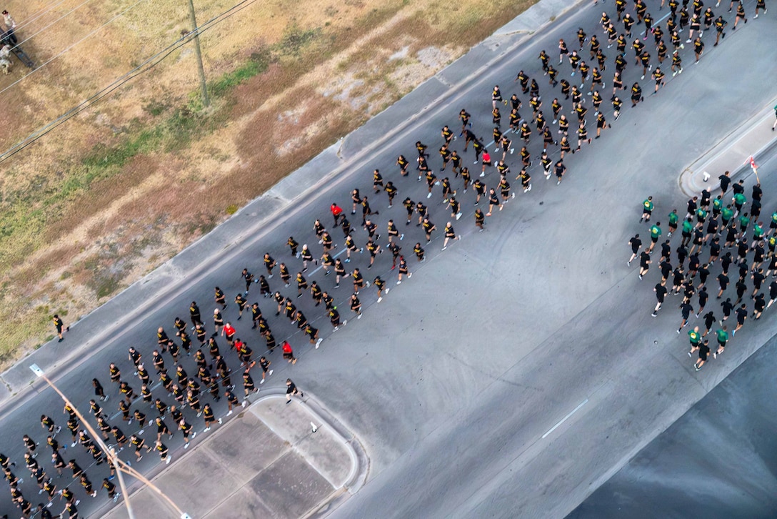 Dozens of soldiers in black athletic gear run in formation in a street as seen from above.