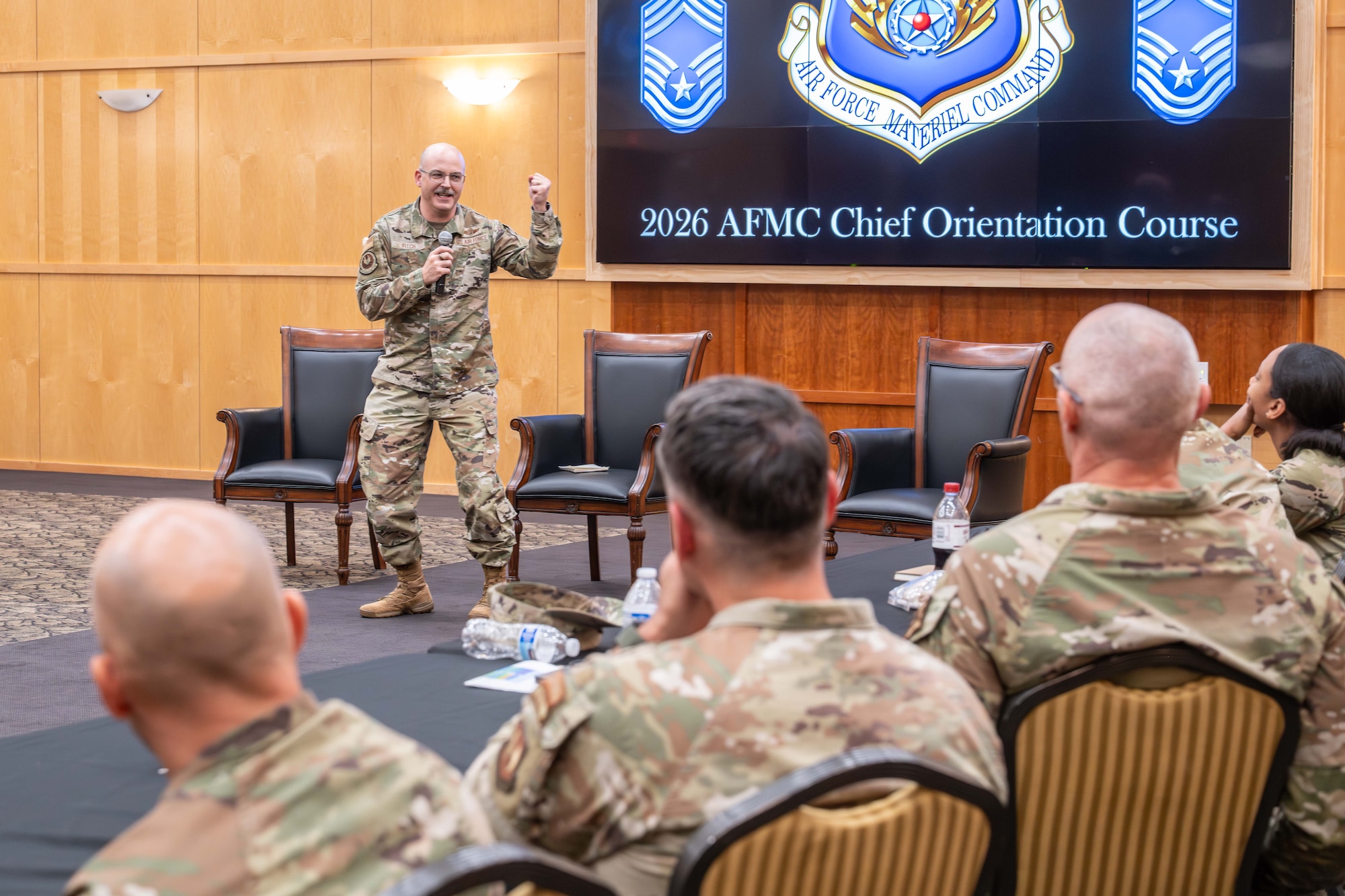 Chief Master Sgt. James “Bill” E. Fitch II, Air Force Materiel Command command chief, stands in front of senior enlisted leaders with his left hand raised in a fist while delivering.remarks.
