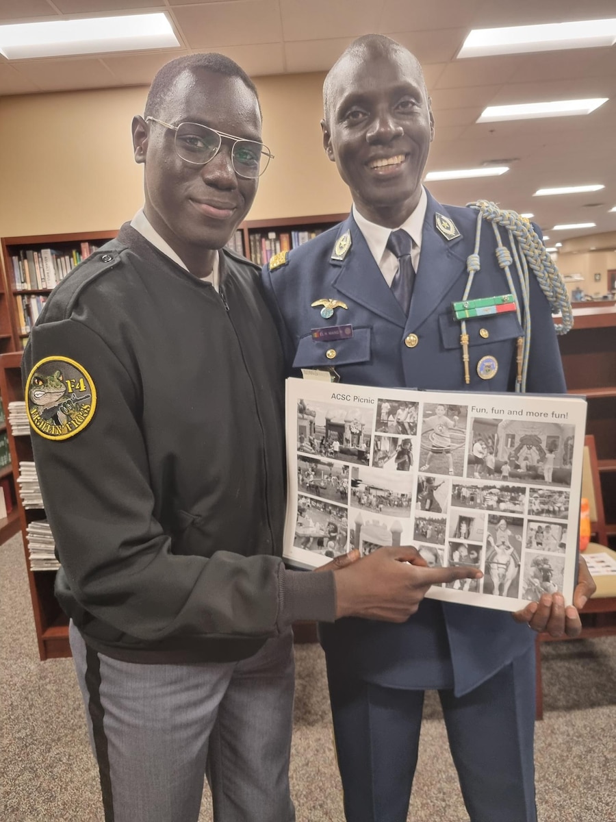 Two persons standing side by side. One is holding a yearbook and the other is pointing to their picture in the yearbook