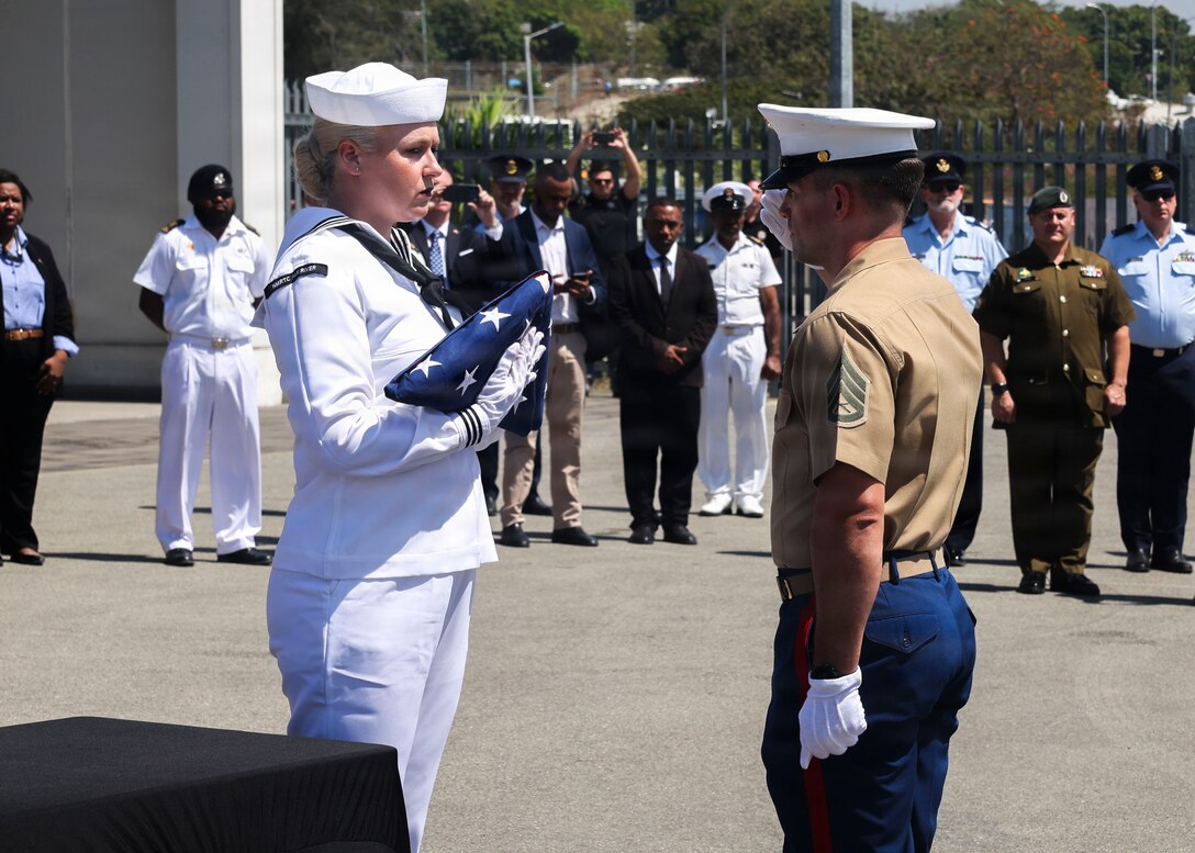 U.S. Marine Corps Staff Sgt. Seth Garner, 1st Explosive Ordnance Disposal Company eod technician (right), salutes U.S. Navy Petty Officer 1st Class Sarah Hoerlein, Navy Medicine Readiness & Training Command Patuxent River hospital corpsman (left), prepares to pass the U.S. flag during the 26-2PG repatriation ceremony