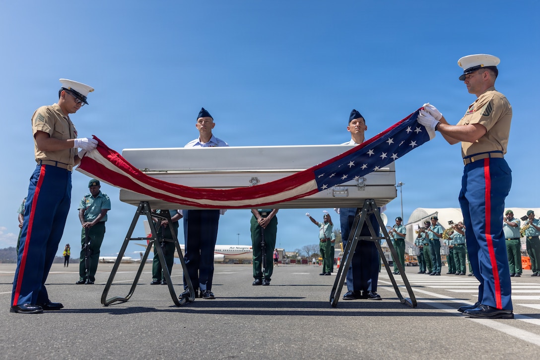 U.S. Marine Corps Staff Sgt. Seth Garner, 1st Explosive Ordnance Disposal Company eod technician (right), and U.S. Marine Corps Sgt. Isaac Jacuinde, Defense POW/MIA Accounting Agency field radio operator (left), unfurl the United States flag