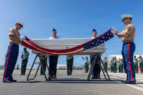 U.S. Marine Corps Staff Sgt. Seth Garner, 1st Explosive Ordnance Disposal Company eod technician (right), and U.S. Marine Corps Sgt. Isaac Jacuinde, Defense POW/MIA Accounting Agency field radio operator (left), unfurl the United States flag