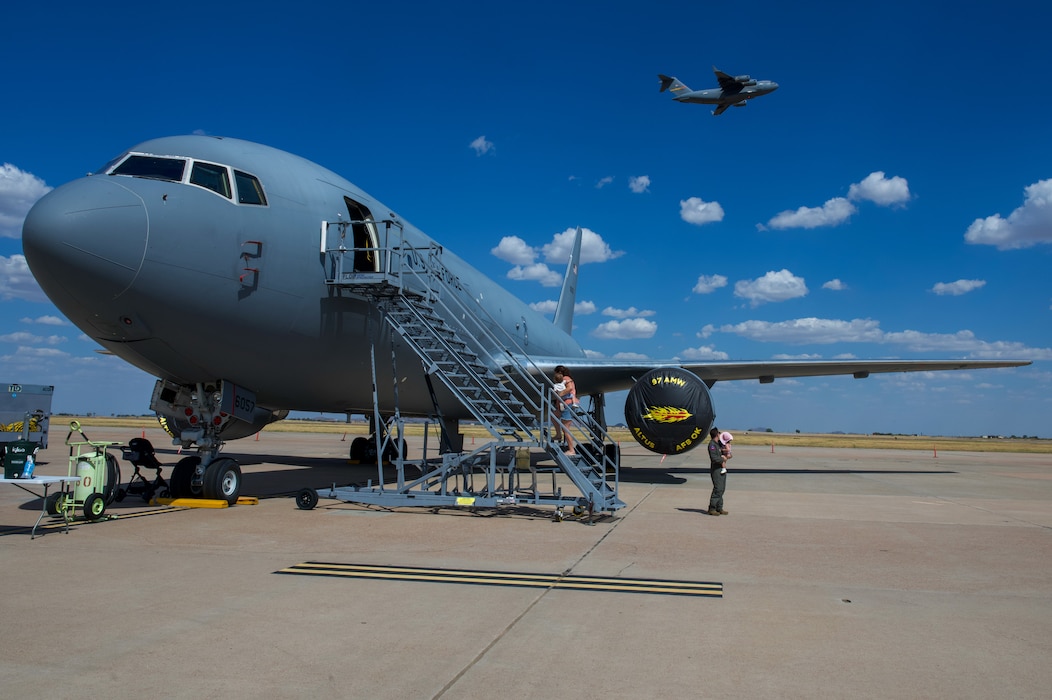 A family boards a U.S. Air Force KC-46 Pegasus static display as a C-17 Globemaster III takes off during the KC-135 70th anniversary celebration at Altus Air Force Base, Oklahoma, Aug. 31, 2026. Families had the opportunity to tour the aircraft to learn more about the base's mission. (U.S. Air Force photo by Airman Elijah Likowski)