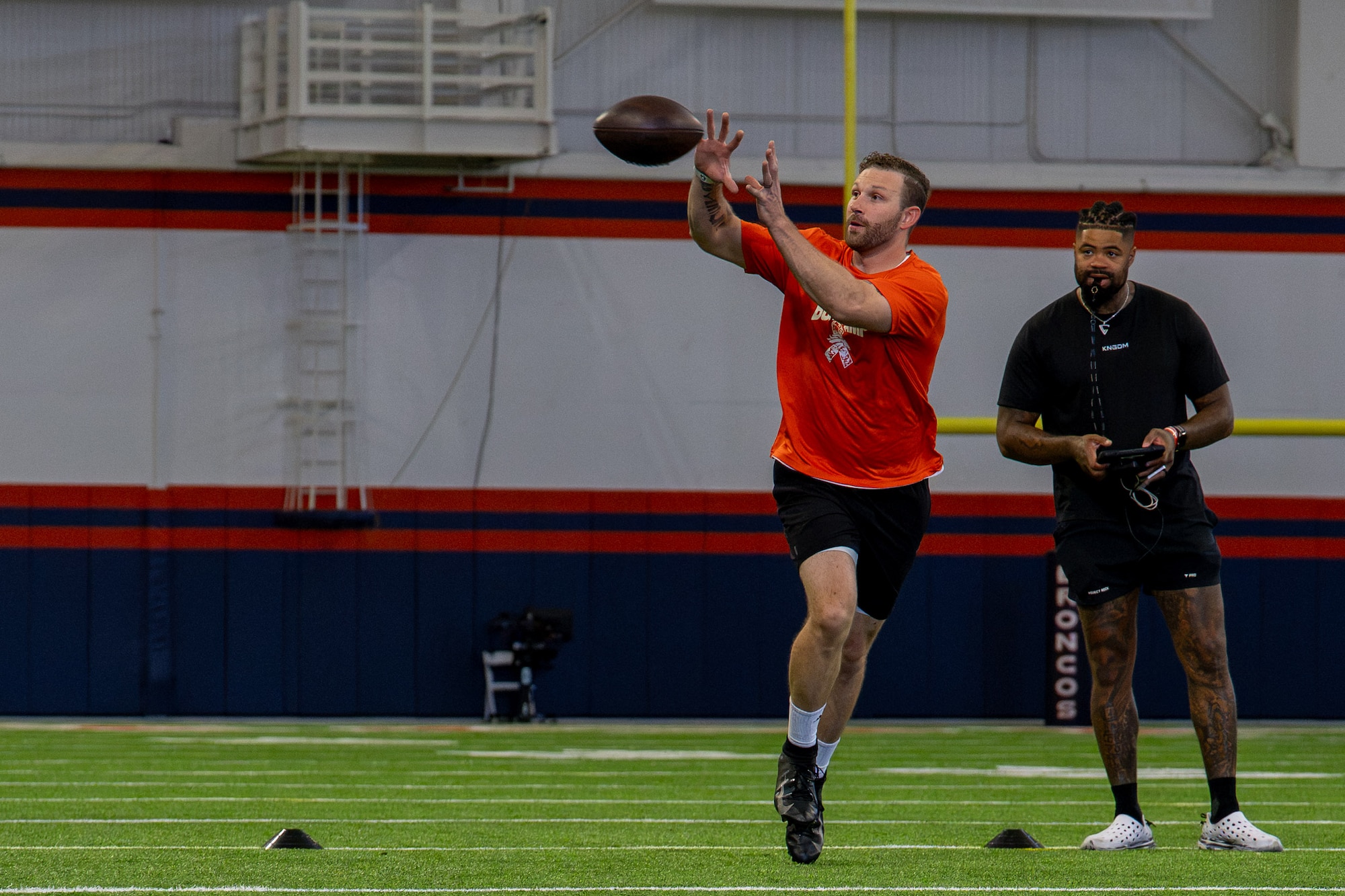 Man catches a football while a man stands behind him with a clipboard