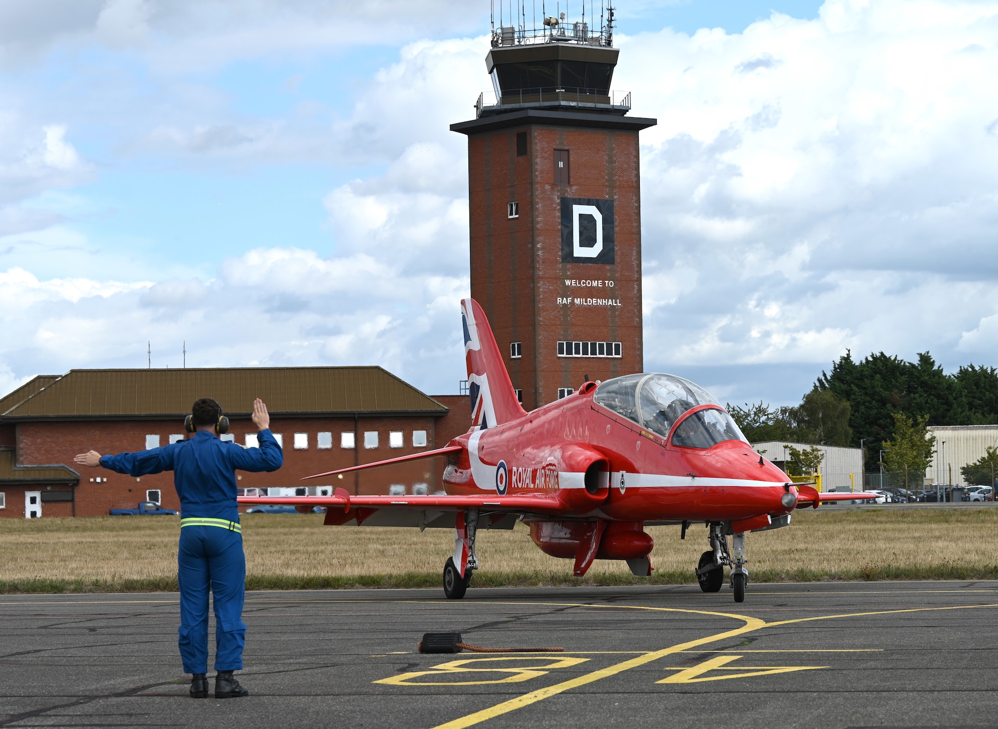 A member of the Royal Air Force Aerobatic Team’s travelling support crew, “Circus,” marshals a Hawk T1 aircraft into its parking spot at RAF Mildenhall, England, Aug. 28, 2026. The Red Arrows performed their famous aerial demonstrations at airshows throughout the UK. (U.S. Air Force photo by Karen Abeyasekere)
