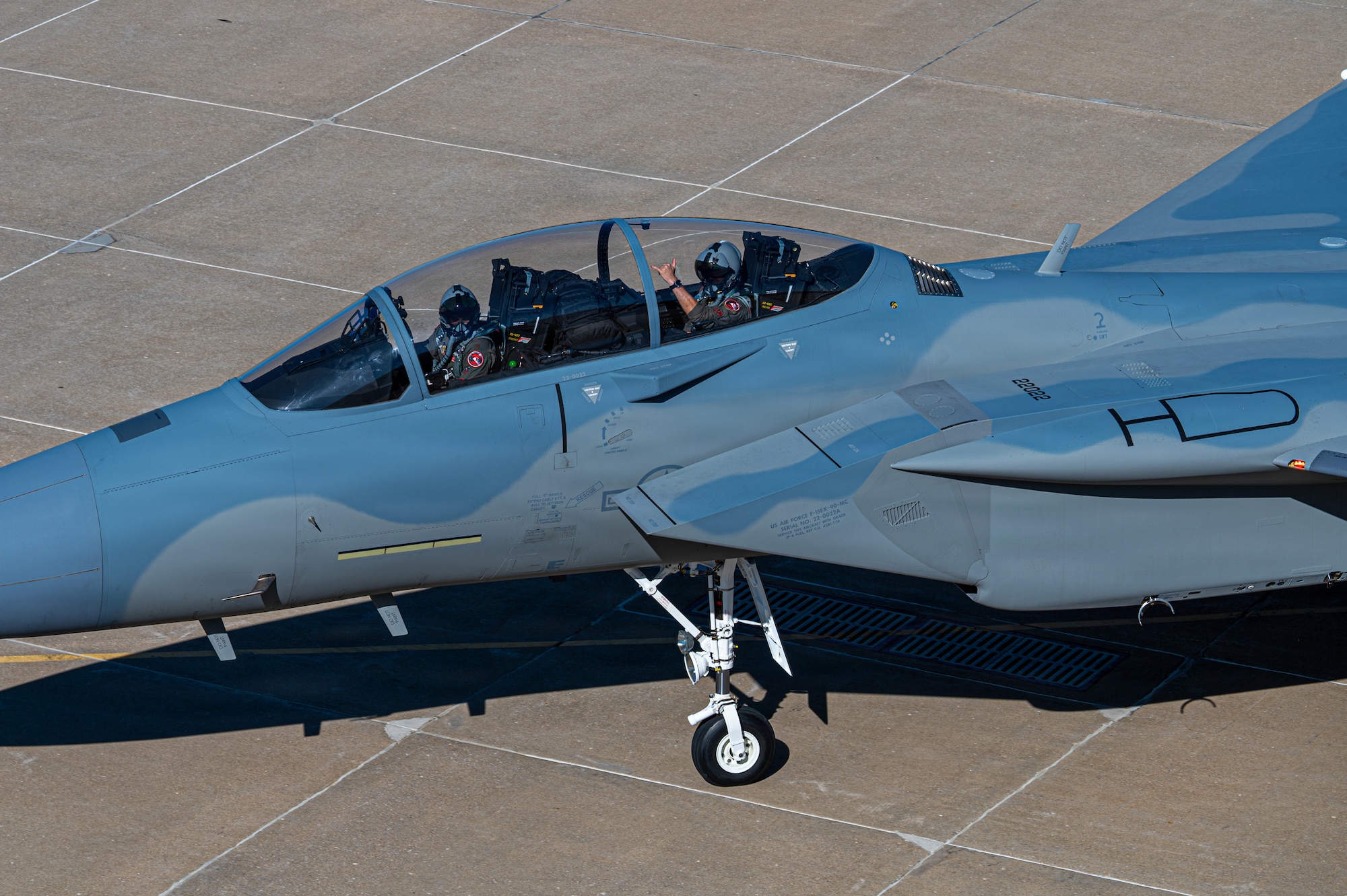 top down view of a jet aircraft as it taxis to a runway while pilots wave