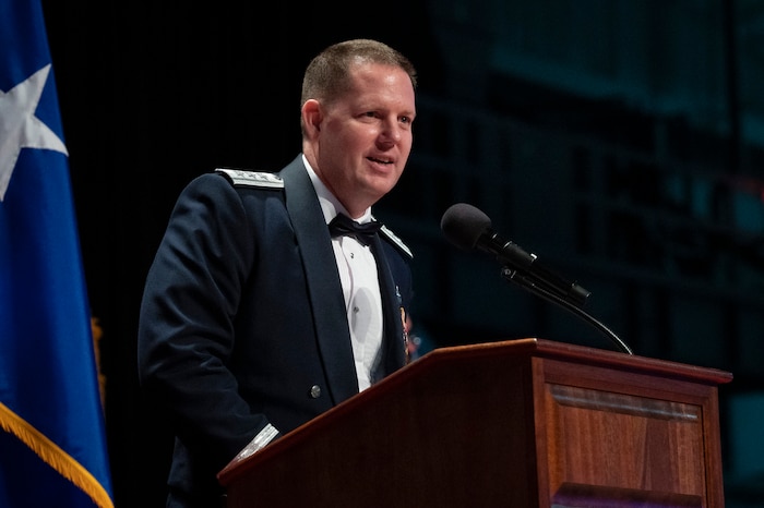Male USAF general wears formal uniform and stands behind a podium giving a speech.