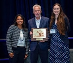 Representing the research team from the U.S. Air Force 59th Medical Wing at Joint base San Antonio-Lackland, Texas, Tarjani Shukla (left), lead bioinformatics and diagnostics research scientist, and Lauren Cornell (right), lead scientist of diagnostics and therapeutics for the Joint Integrative Clinical Medicine research directorate, accept the Young Investigator competition’s second place award for a poster presentation titled, “Effectively Screening Bedtime Procrastination & Smartphone Use Among Active Duty Service Members: A Quality Improvement Initiative,” at the 2026 Military Health System Research Symposium in Kissimmee, Florida, Aug. 6. The competition honored early-career researchers for their innovative studies of warfighter health and readiness. Presenting the award is Dr. Terry Rauch, acting deputy assistant secretary of war for health readiness policy and oversight.