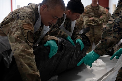 U.S. Air Force Tech. Sgt. Doddy Burhannudin (left) a resource management technician assigned to the 436th Force Support Squadron, and U.S. Marine Anderson Pachecoguevara, a personnel retrieval and processing specialist assigned to PRP Company, 4th Combat Readiness Regiment, lift a training dummy inside a human remains pouch as part of the re-icing procedures at Grayling Army Airfield, Michigan, during Exercise Northern Strike 26-2, Aug. 8, 2026.