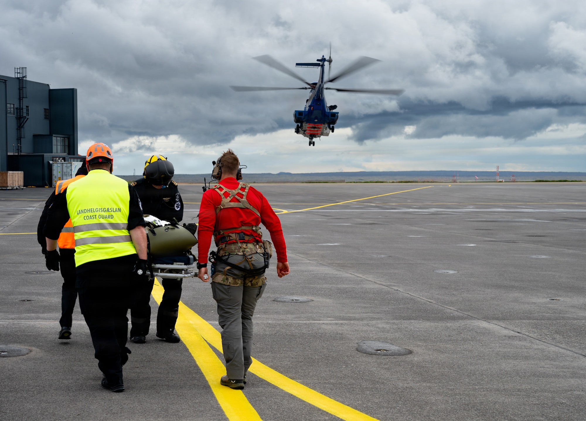 U.S. Air Force pararescuemen assigned to the 38th Rescue Squadron and Icelandic Coast Guard personnel transport a simulated casualty as an Icelandic Coast Guard Airbus H225 Super Puma departs during an artificial mass casualty scenario as part of exercise Northern Viking 26 at Keflavík Air Base, Iceland