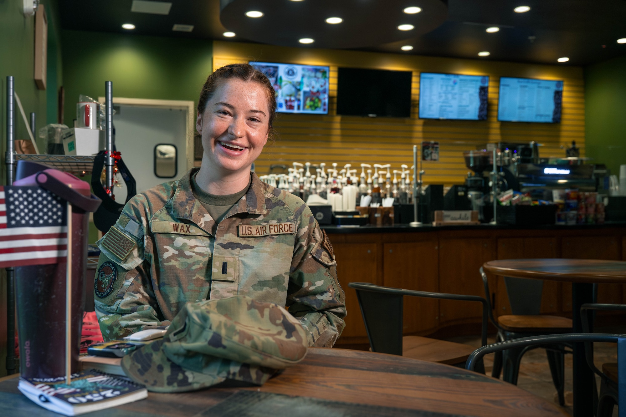 Alt Text: A photo of a service member smiling while sitting inside of a coffee shop.