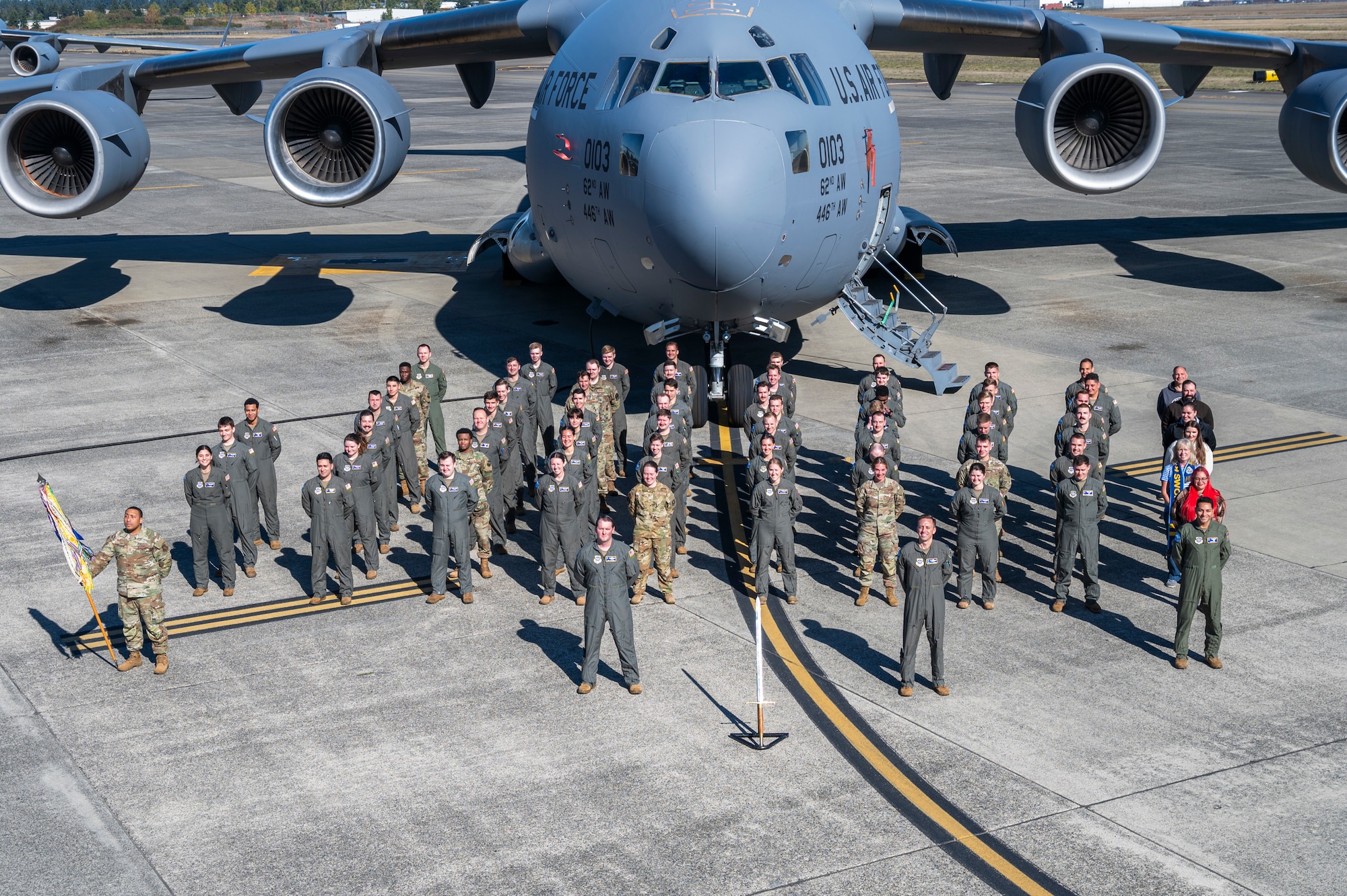 A group of people stand in formation in front of a plane.