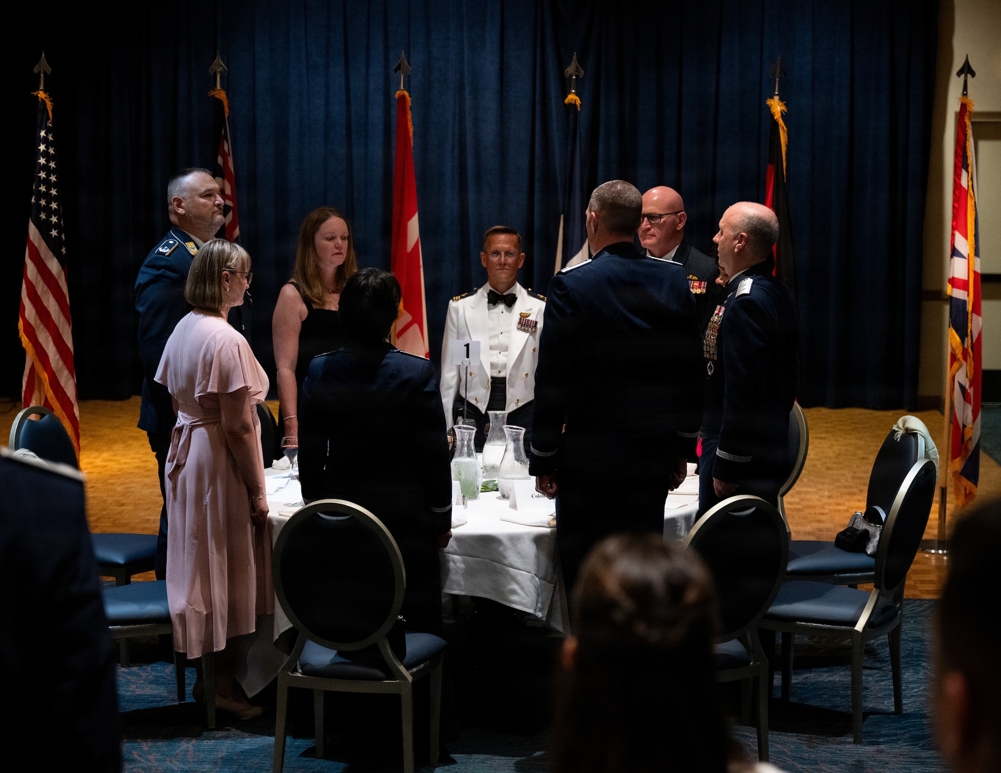 Servicemembers and their spouses stand at attention during an anthem.