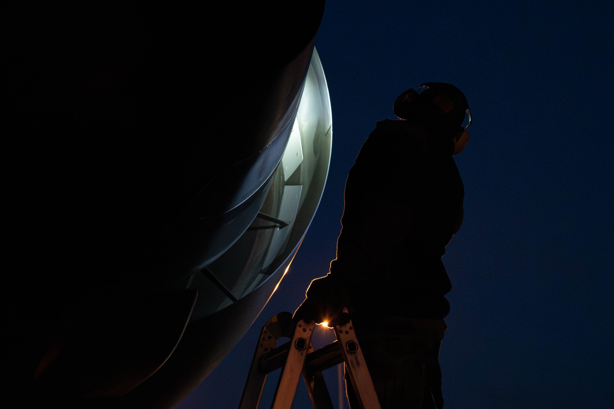 A person on a ladder uses a flashlight to view an aircraft engine up close.