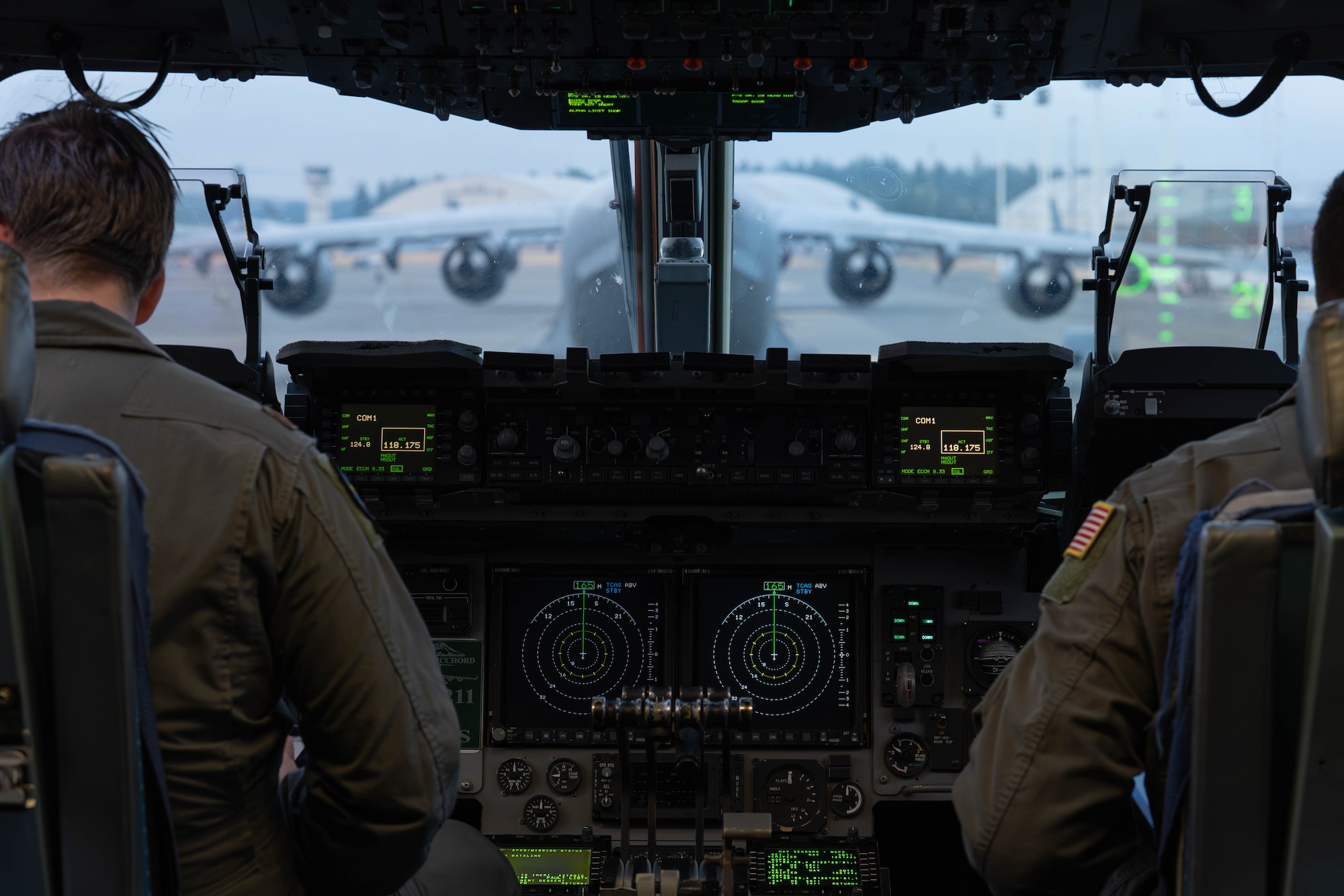 Two people sit in the flight deck of an aircraft.