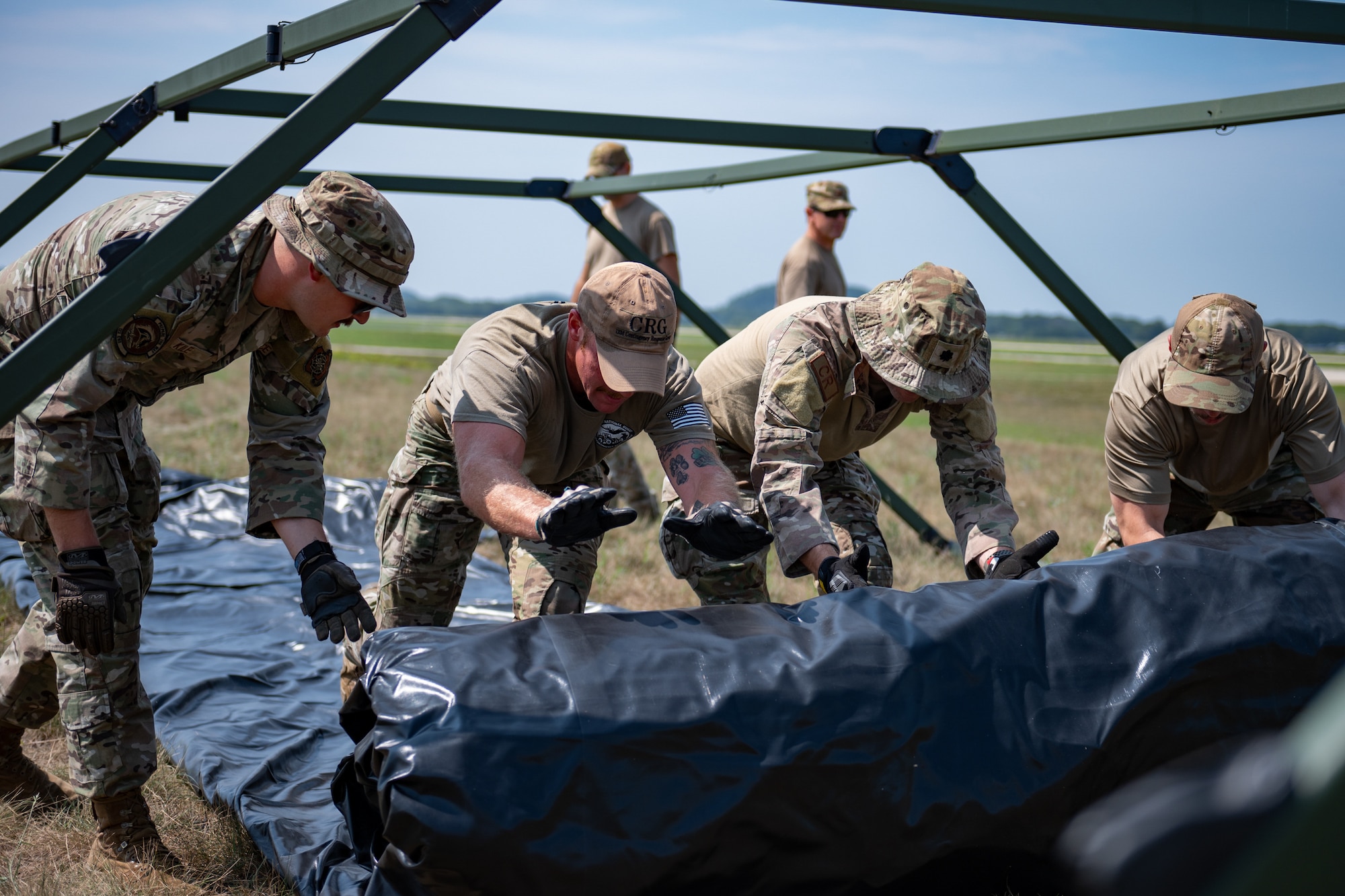 U.S. Air Force Staff Sgt. Thomas Kile, Master Sgt. Dylan Rhodes, Lt. Col. Brian Stoops and Senior Airman Micah Tungate of the Kentucky Air National Guard’s 123rd Contingency Response Group unravel a tent cover during camp setup for exercise Patriot 2026 at Volk Field Combat Readiness Training Center, Wis., Aug. 20, 2026. Patriot 26, an Air National Guard-hosted exercise brings together approximately 1,000 Airmen and Soldiers from National Guard units across 35 states, along with federal, state and local agencies, to enhance domestic response readiness and interagency coordination during large-scale emergencies. (U.S. Air National Guard photo by Senior Airman Angelee Barnett)