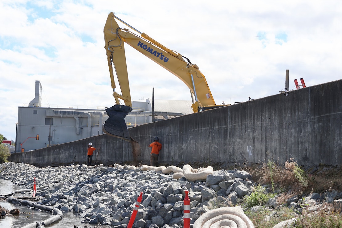Photo of workers wearing safety hats and vests repairing a levee.