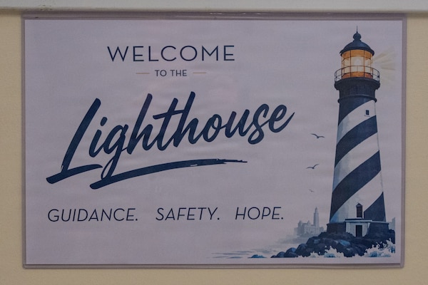 A sign that says "Lighthouse" hands on a white wall.