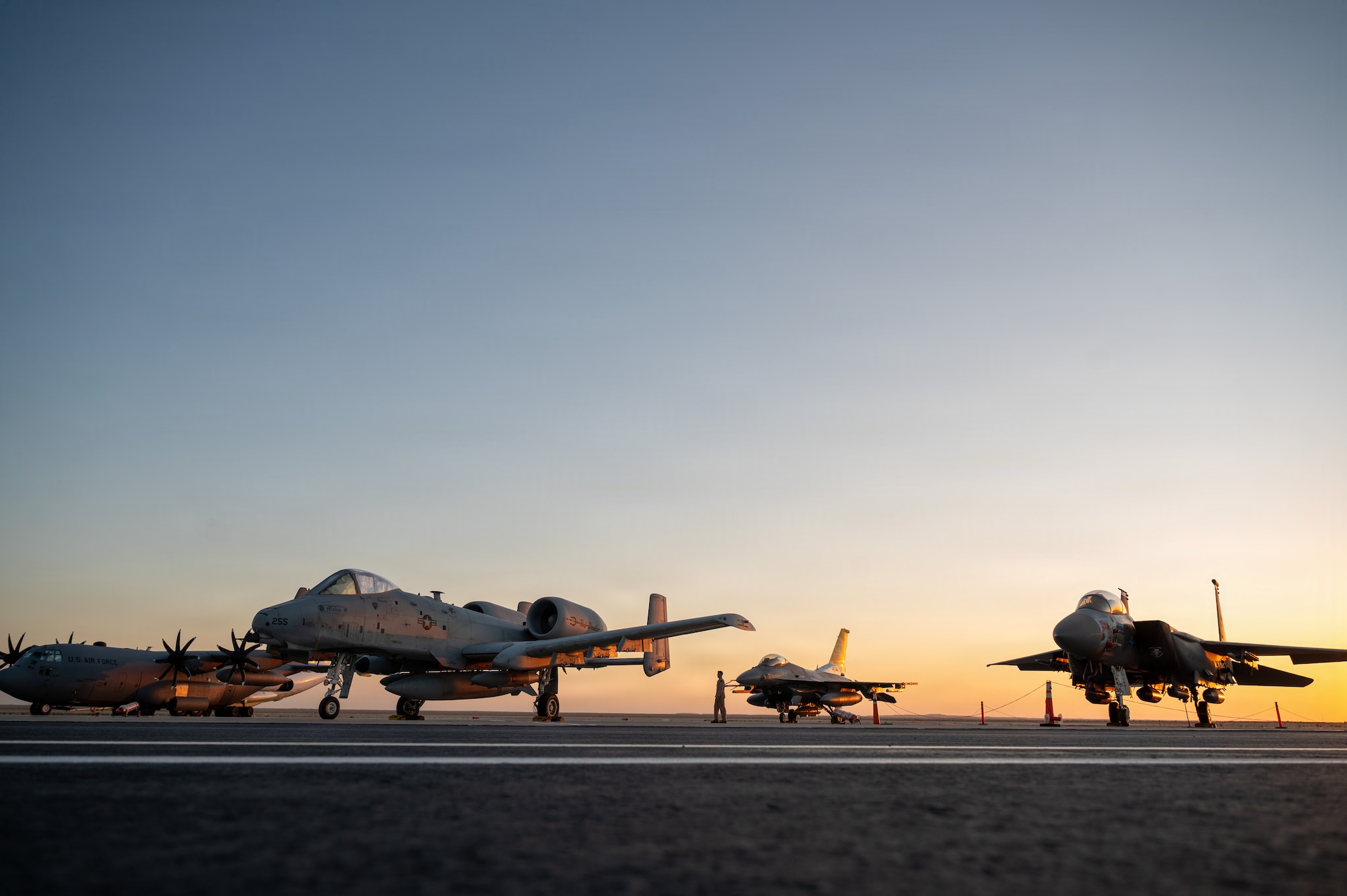a sun sets behind aircraft on a flightline
