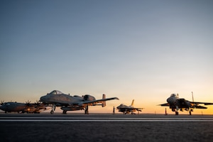 a sun sets behind aircraft on a flightline