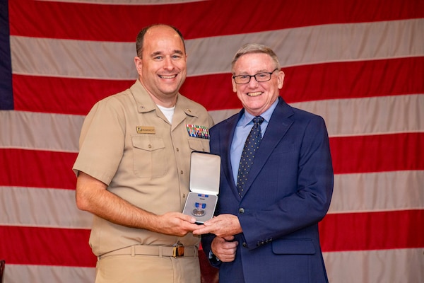 Cmdr. Joseph Fromknecht, a deputy chief of staff assigned to Naval Medical Forces Atlantic, presents Dennis Connell, a secretary with NMFL, and a native of Rensselaer, New York, with a Meritorious Civilian Service Award during Connell’s retirement ceremony on board Naval Support Activity (NSA) Hampton Roads - Portsmouth Annex, Portsmouth, Virginia, Aug. 28, 2026. One of the Navy’s highest civilian honors, the award recognized Connell’s contributions during 21 years with NMFL and 41 years total of public service. (U.S. Navy photo by Mass Communication Specialist 2nd Class Levi Decker)