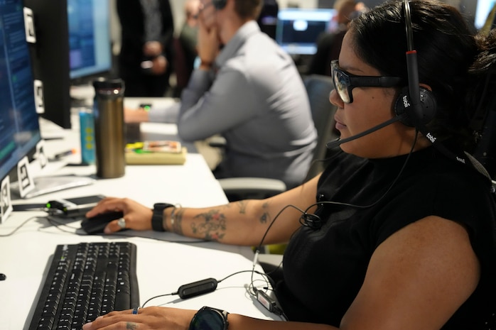 a woman wearing a headset, specialty glasses and watch works at a computer.
