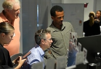 a group of people stand behind observing a civilian working on a computer