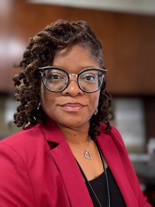 Smiling woman with black glasses wears a black top and red blazer