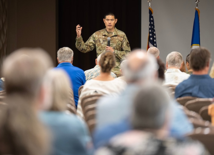 A man in camouflage uniform gestures as he speaks in front of a crowd in civilian clothes.
