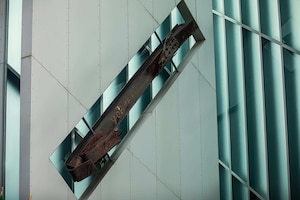 A large piece of metal covered in rust is displayed on large wall.