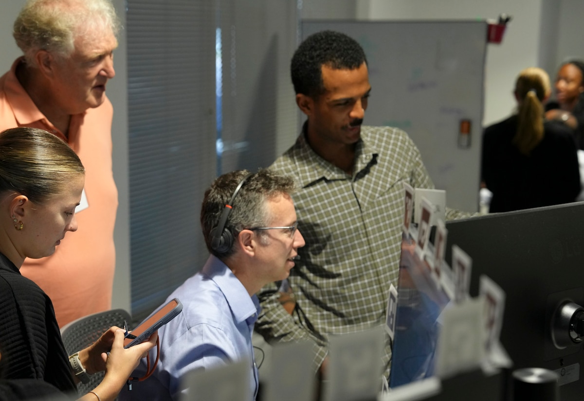 a group of people stand behind observing a civilian working on a computer