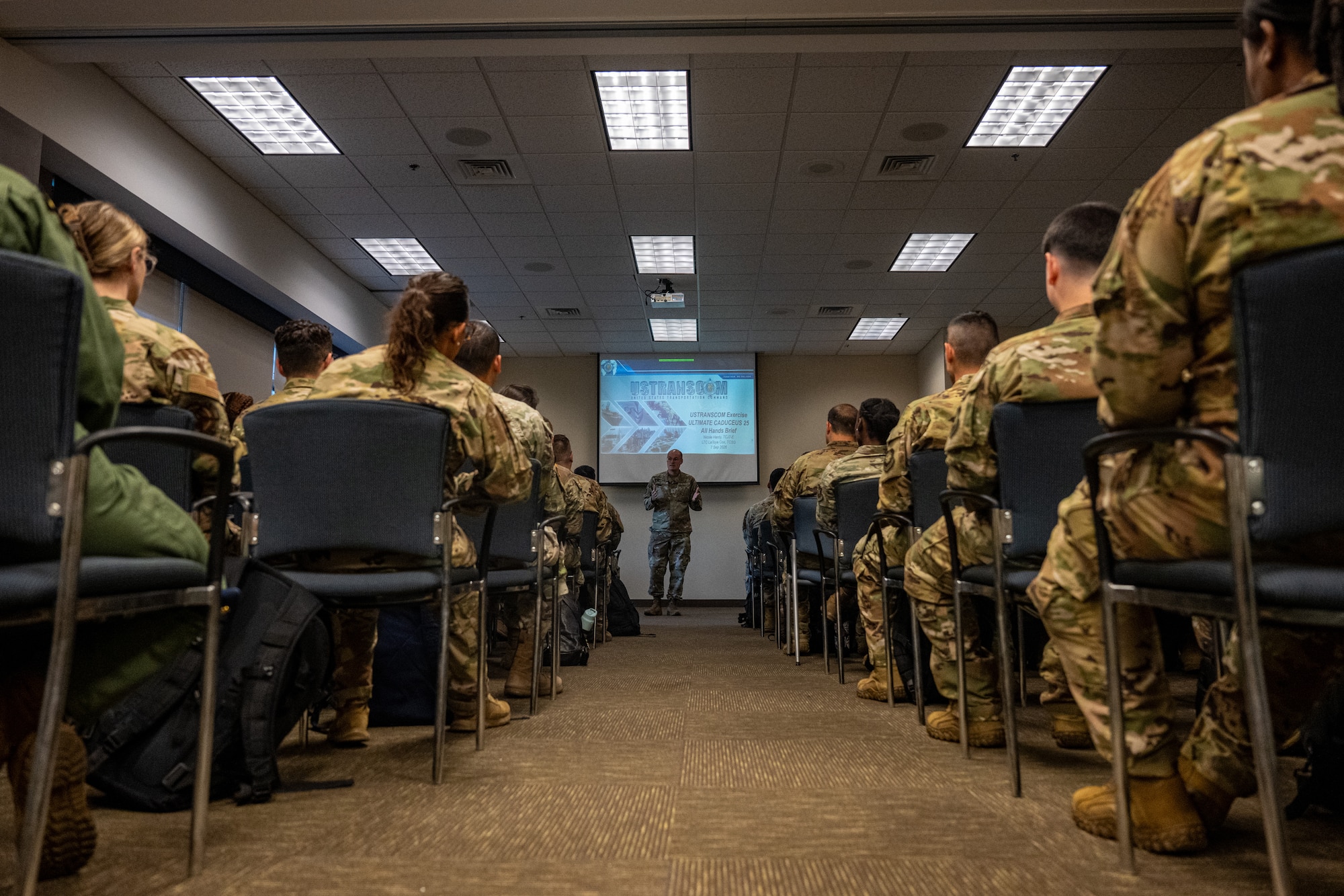 Uniformed service members sit in a classroom facing an instructor who stands at the front of the room and addresses the group during Exercise Ultimate Caduceus 2026.