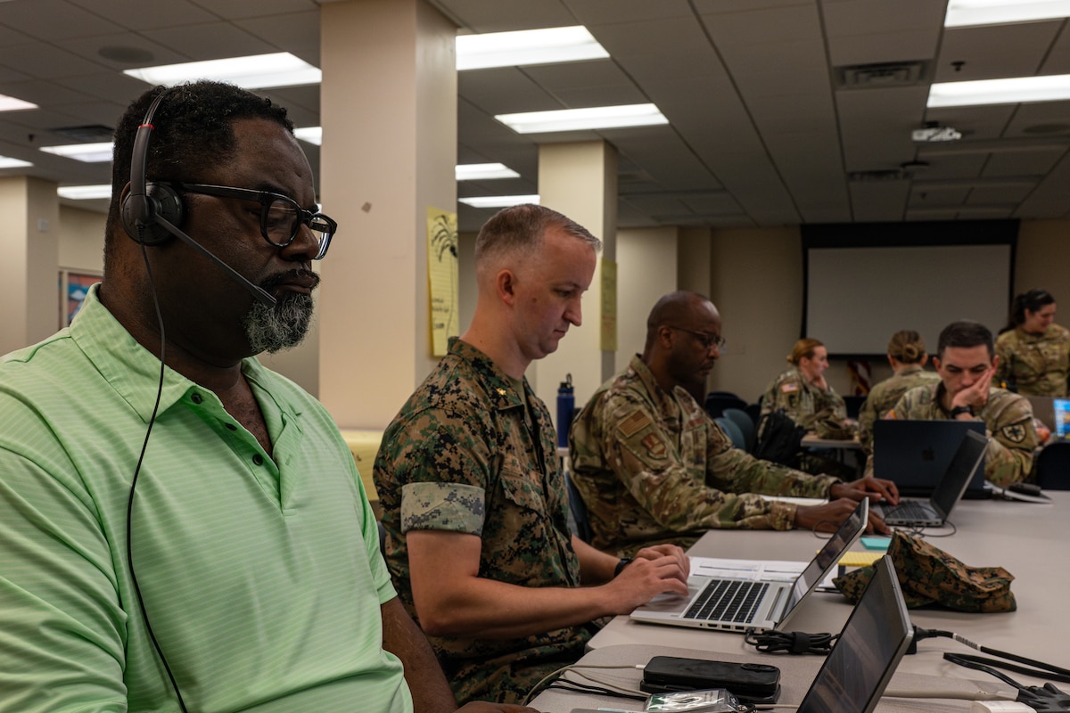 Department of War personnel, including Marine, civilian, Air Force and Army members, work side by side at computer stations, demonstrating interoperability and coordinated communication during Exercise Ultimate Caduceus 2026 at Scott Air Force Base, Illinois.