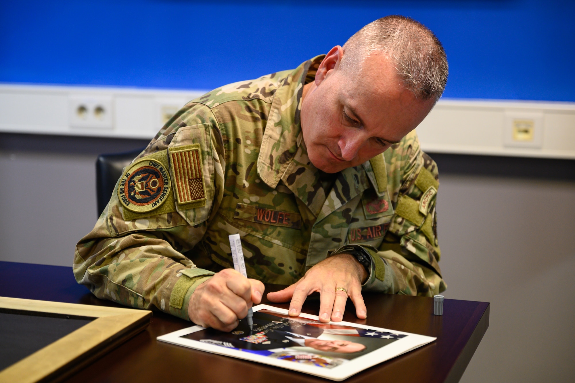 Chief Master Sergeant of the Air Force David Wolfe signs his official portrait for the Pitsenbarger Airman Leadership School's Chiefs' Room during a base visit.