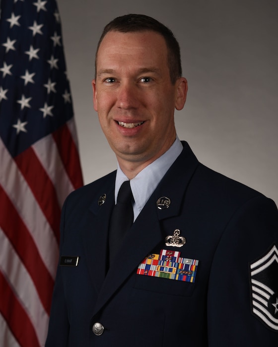 SMSgt Kadow in service dress in front of an American Flag background.