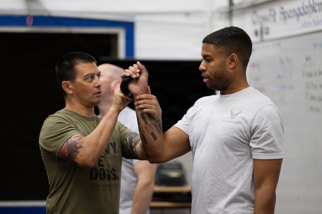 Craig Descoteaux, left, an operational support team strength and conditioning coach, instructs U.S. Air Force Tech. Sgt. John Thomas Larkins III, a 52nd Force Support Squadron financial analysis supervisor, on proper kettlebell technique during Saber Fitness Day.