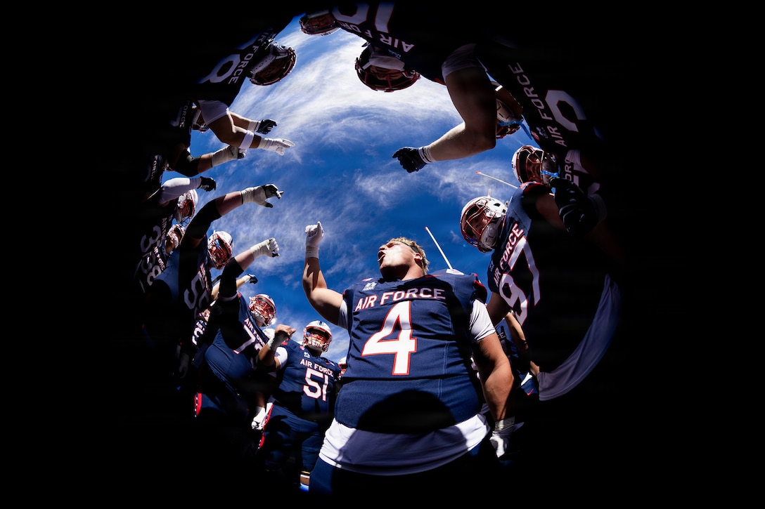 A person in a football uniform holds up his fist and shouts while surrounded by more than a dozen other people in football uniforms.