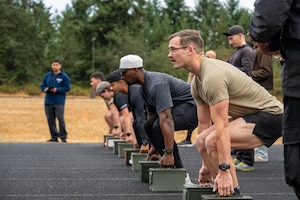 A line of people squat to grasp ammo cans on a running track.