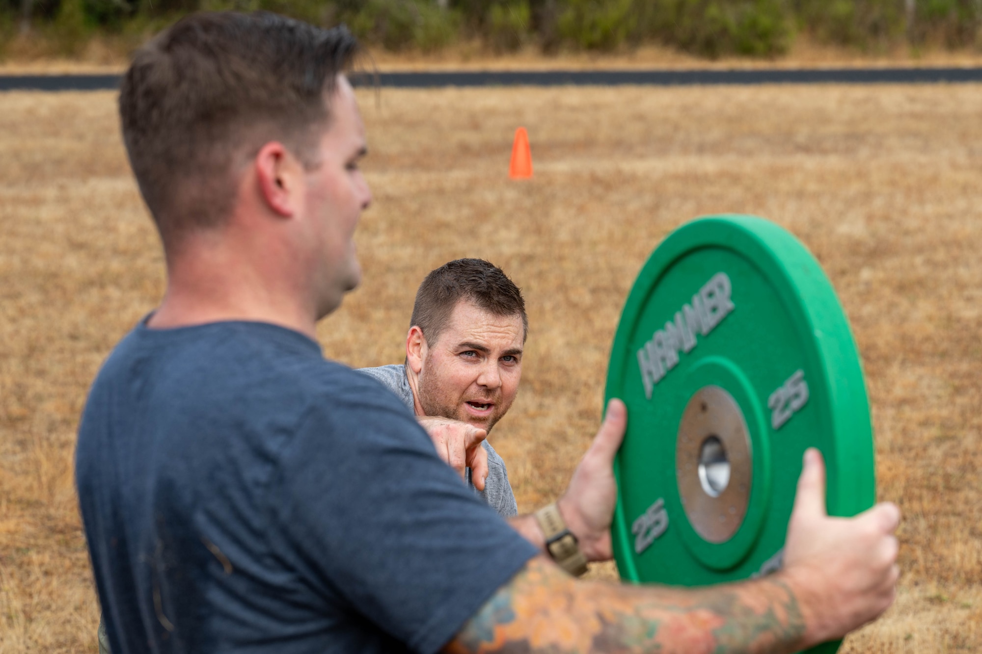 A man points at another man holding a circular weight.