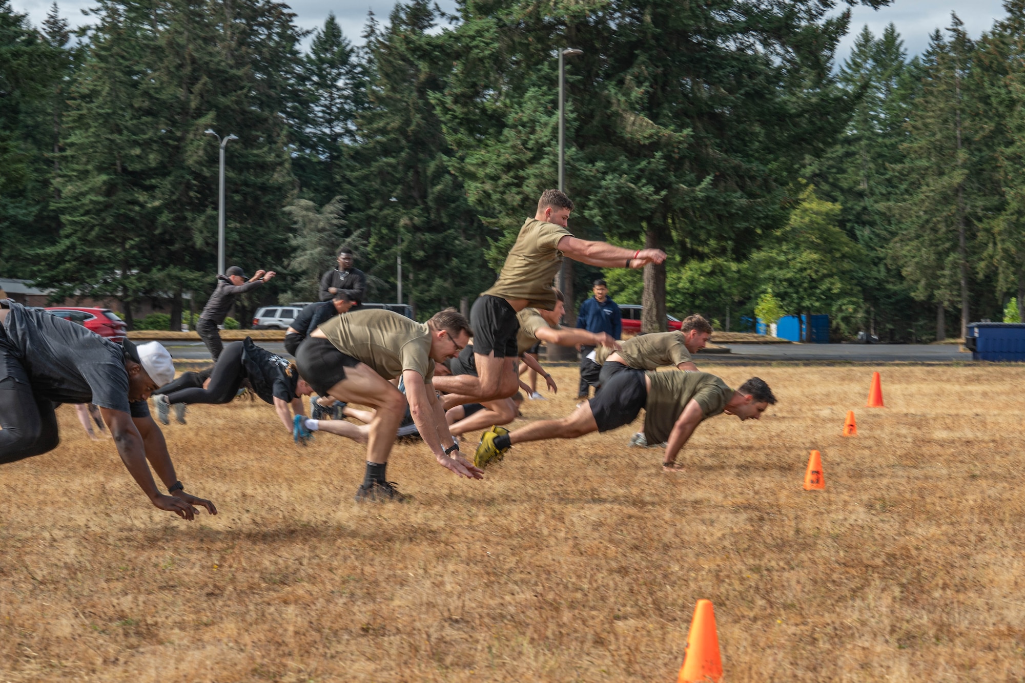 A large group leap towards a line of orange cones in a field.