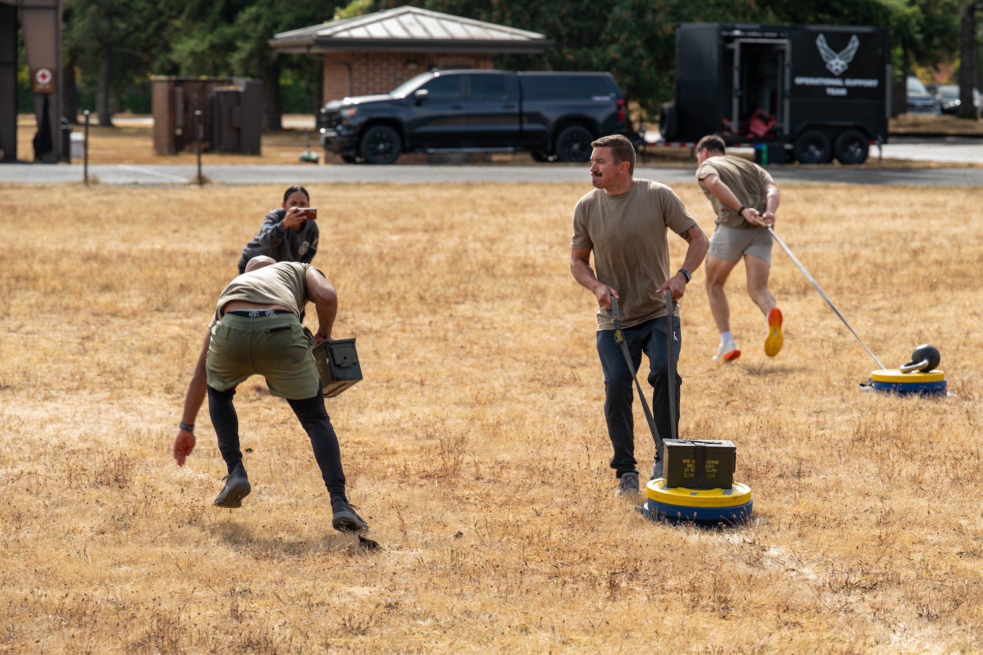 Three people run through a field pulling weights.