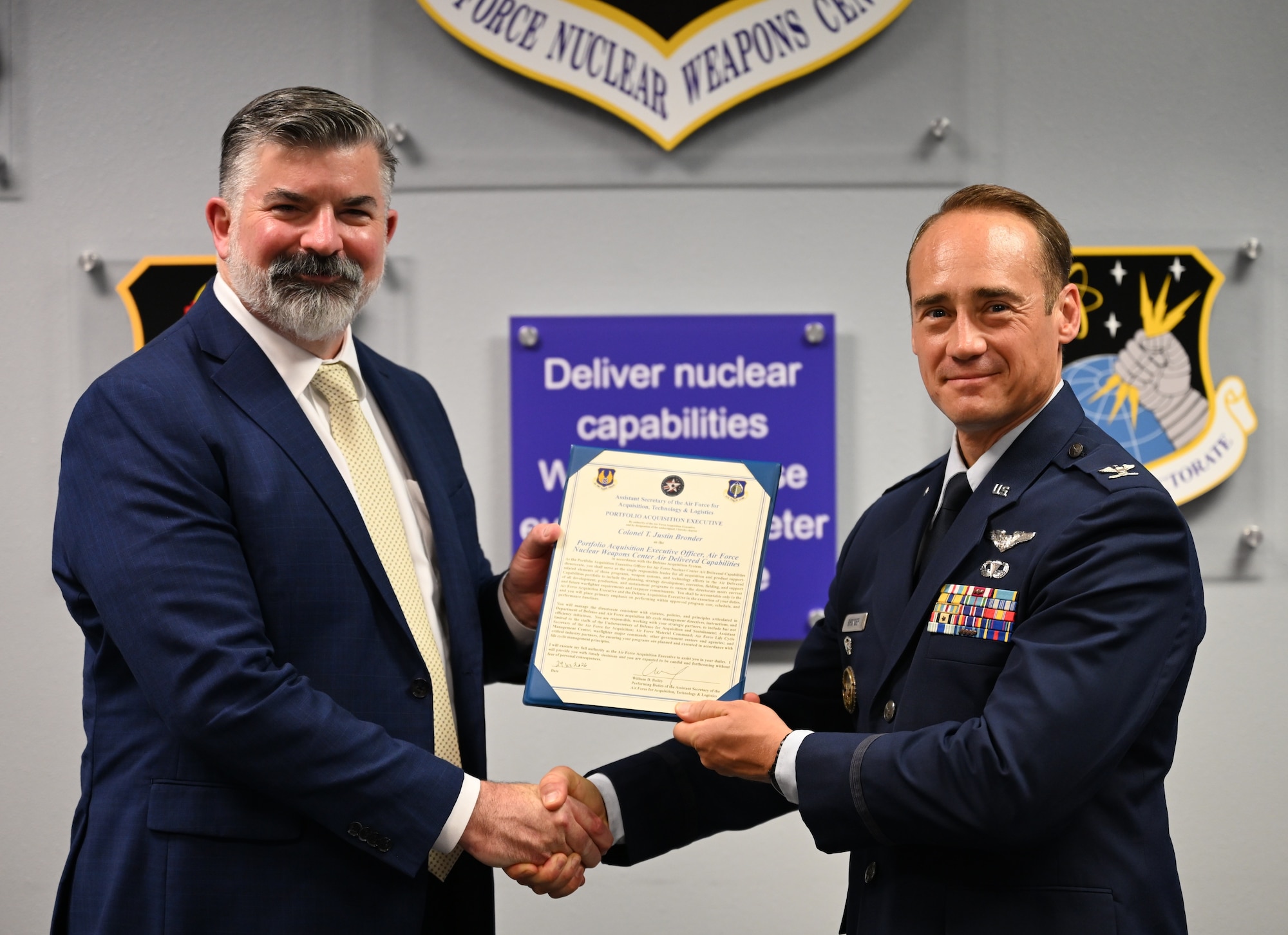 A man in a suit presents a certificate to a man in dress uniform