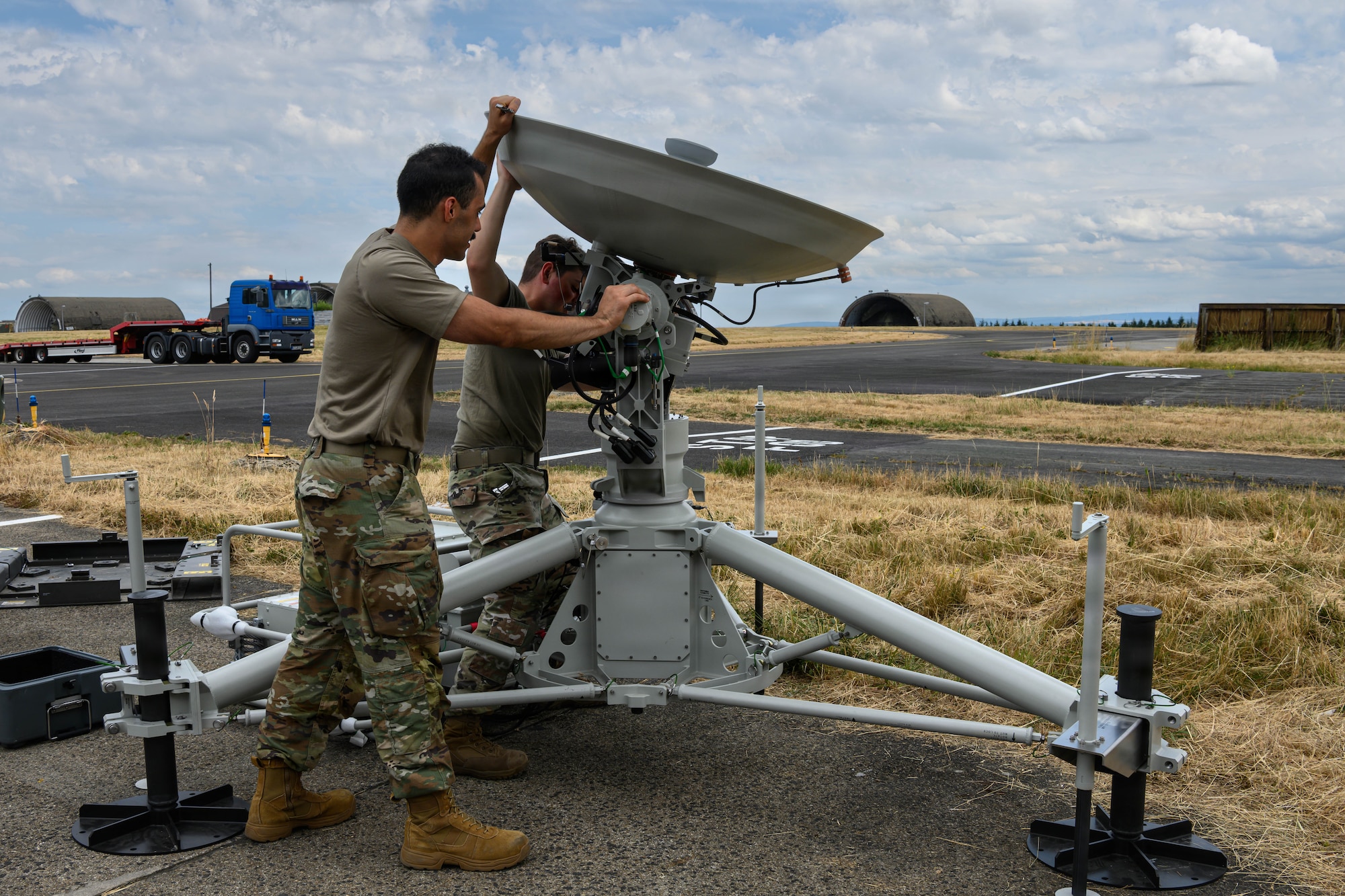 Two U.S. Air Force Airmen adjust a satellite dish.